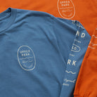 Bay Waves Standard Long Sleeve Shirt - Upper Park Clothing - Blue t-shirt with 'Upper Park' logo on an orange background