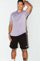 mean leaning against a white wall wearing a orchid simple mineral washed shirt and black men's stadium shorts from Upper Park Clothing