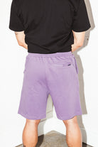 mean leaning against a white wall wearing a black pocket flag and purple stadium shorts from Upper Park Clothing