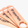 rose gold bottle opener with giant text that says "Upper Park" laying on a flat grey background