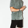 mean leaning against a white wall wearing a green simple mineral washed shirt and black men's stadium shorts from Upper Park Clothing