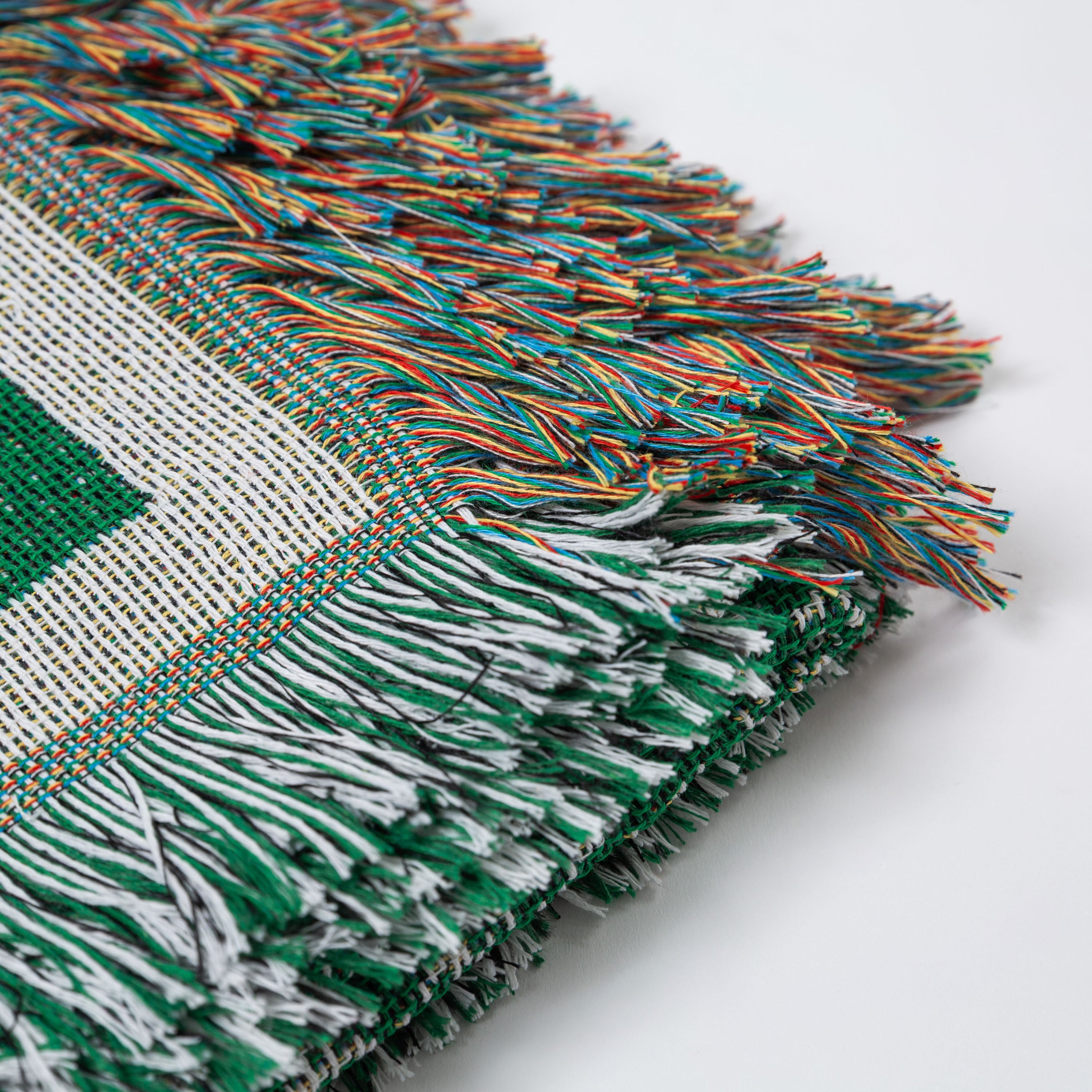 Close-up of a green and white woven fabric with colorful fringe on a light gray background - Upper Bidwell Park Woven Blanket