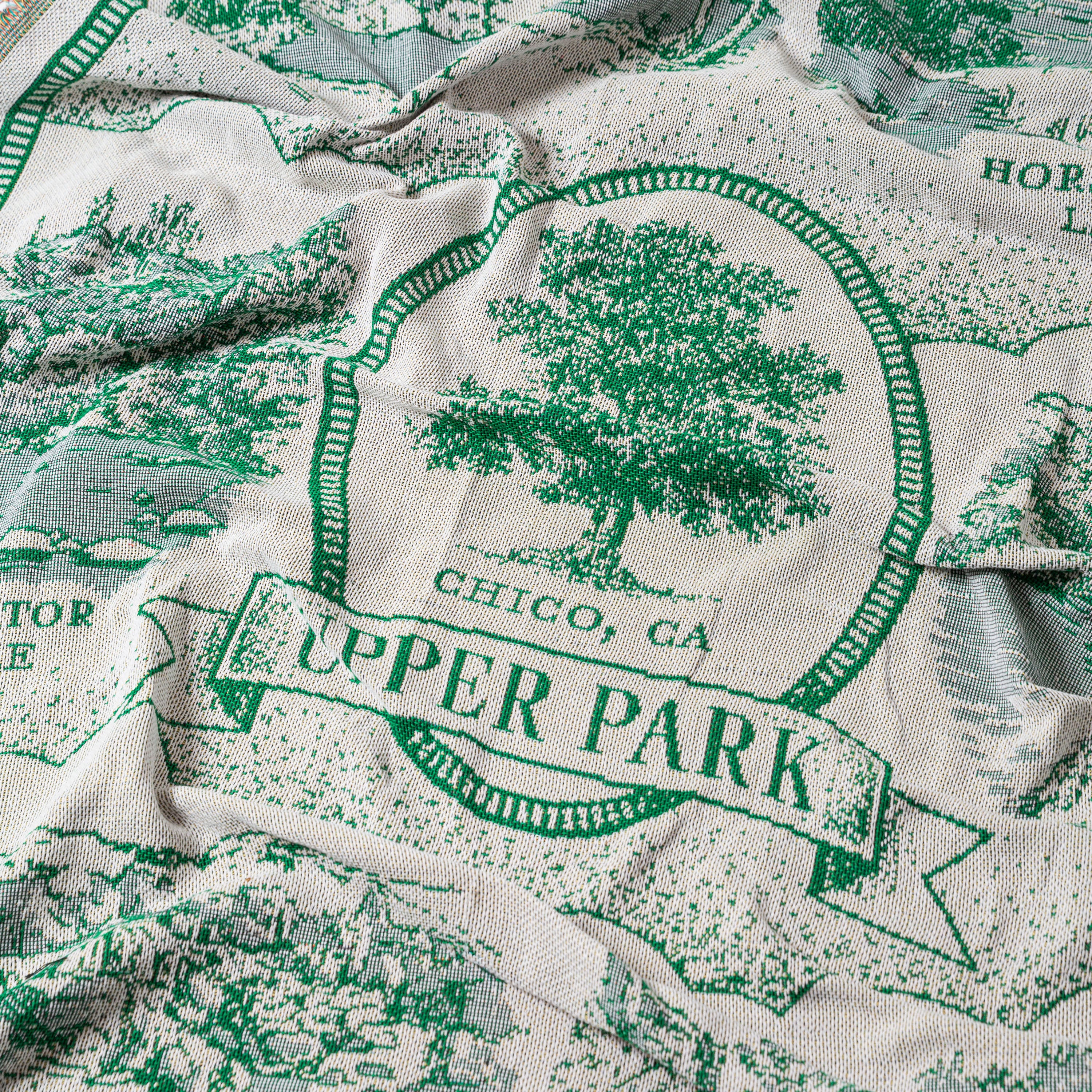 Fabric with green and white design of a tree and text 'Upper Park, Chico, CA'. - Upper Bidwell Park Woven Blanket