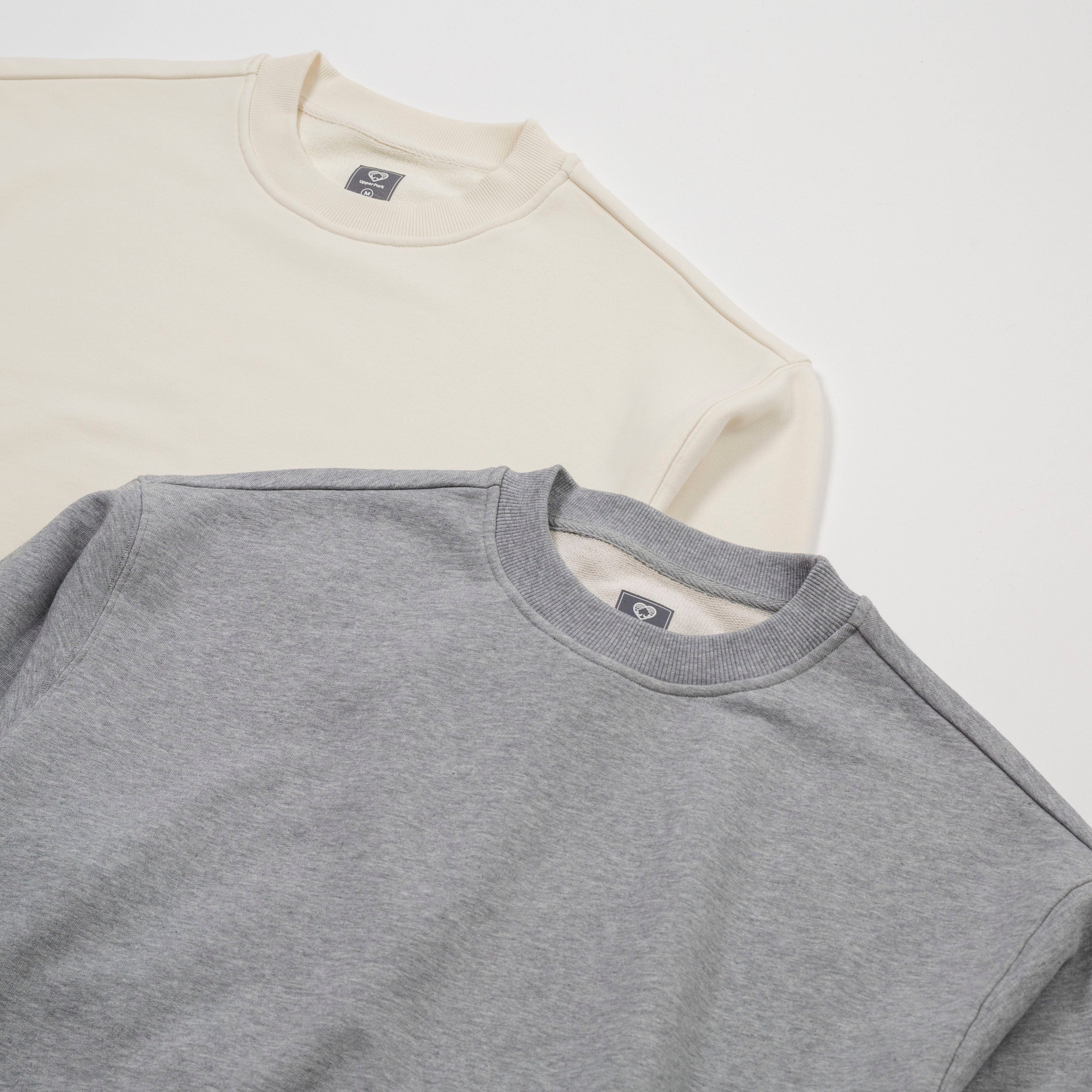 Two folded shirts, one beige and one gray, on a white background. - Basics Premium Cotton Sweater