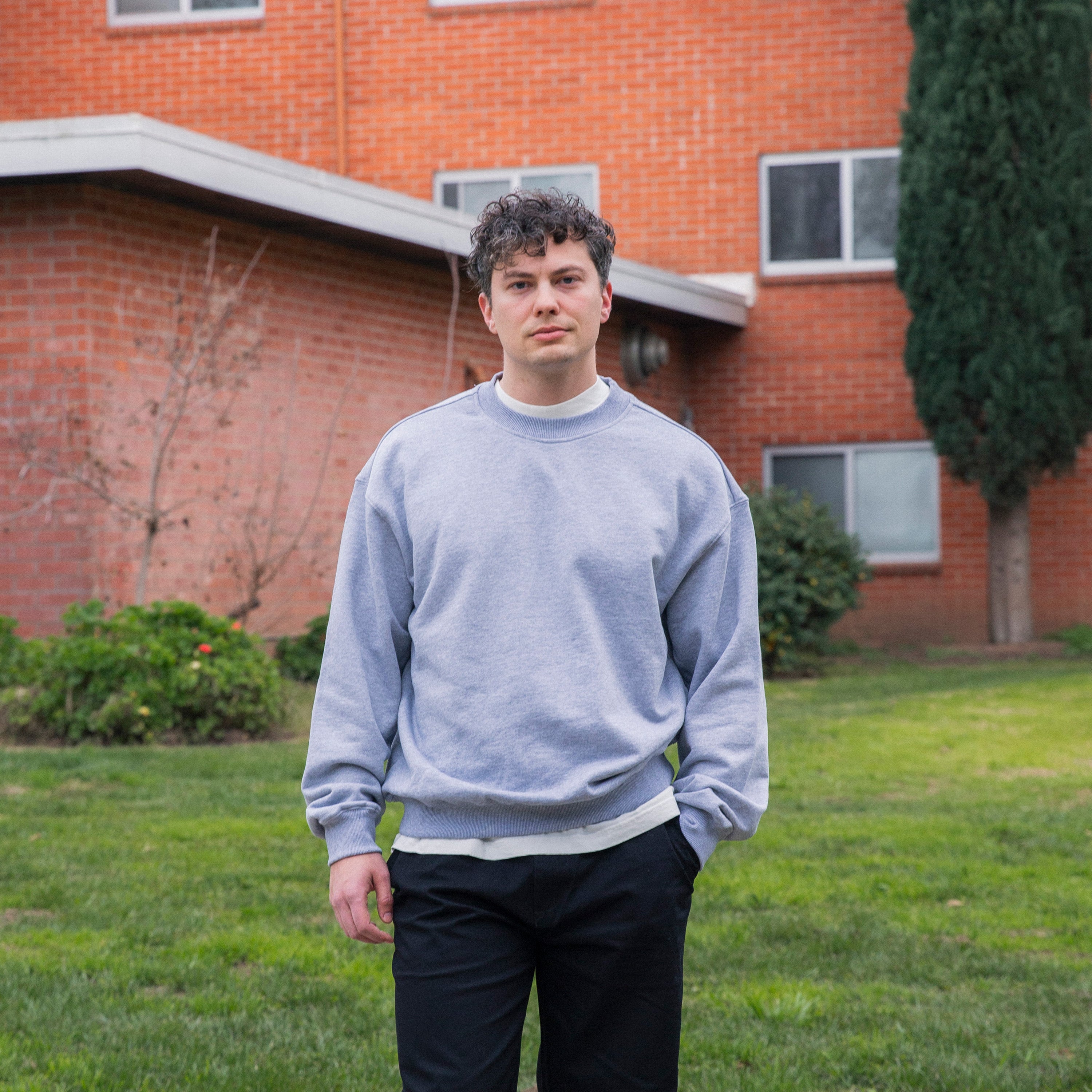 Person wearing a light blue sweatshirt standing in front of a brick building - Basics Premium Cotton Sweater
