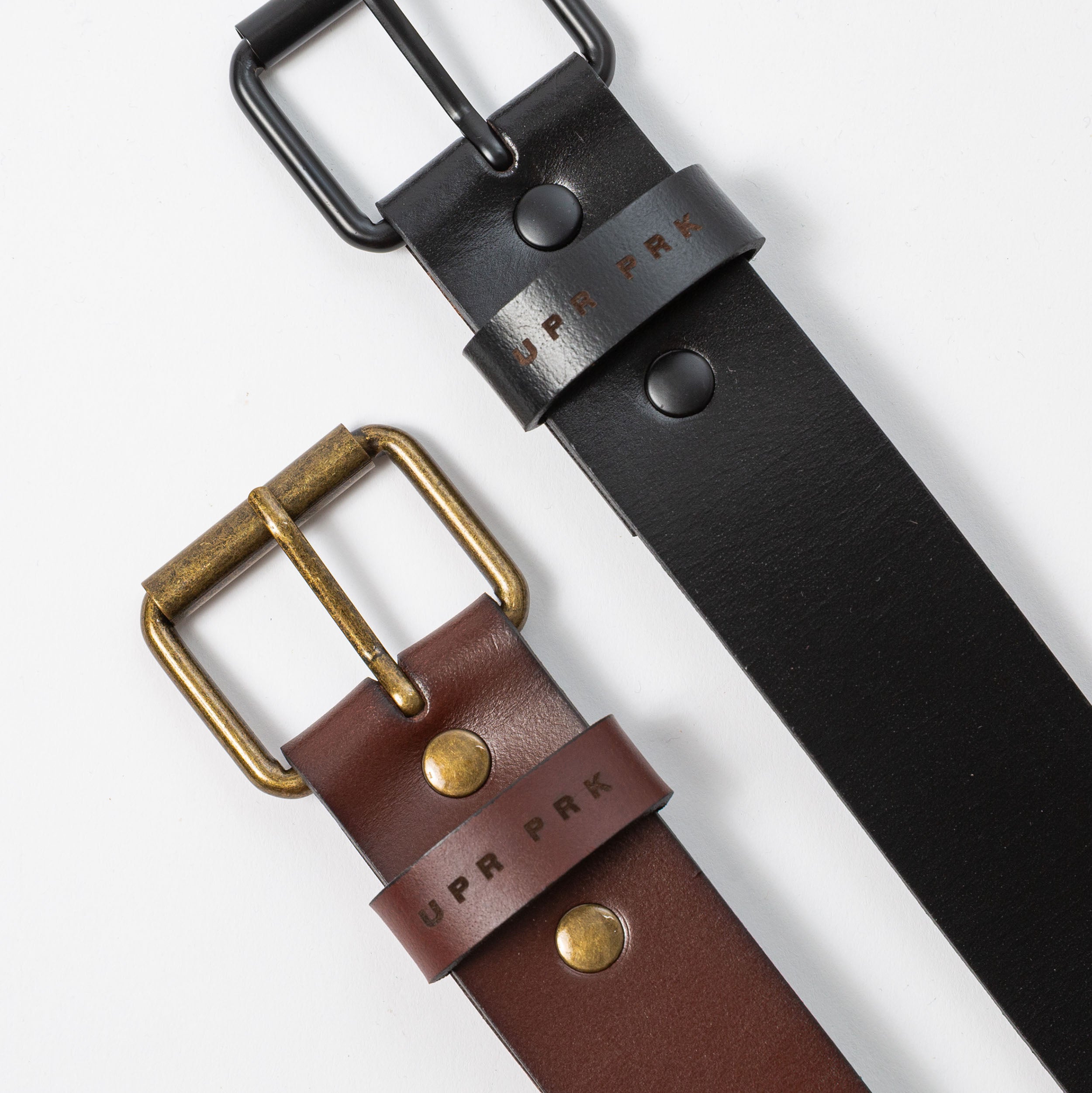 A brown and black leather belt with metal belt buckles on a white background - UPR PRK etched into the leather - Upper Park Basic Leather Belt