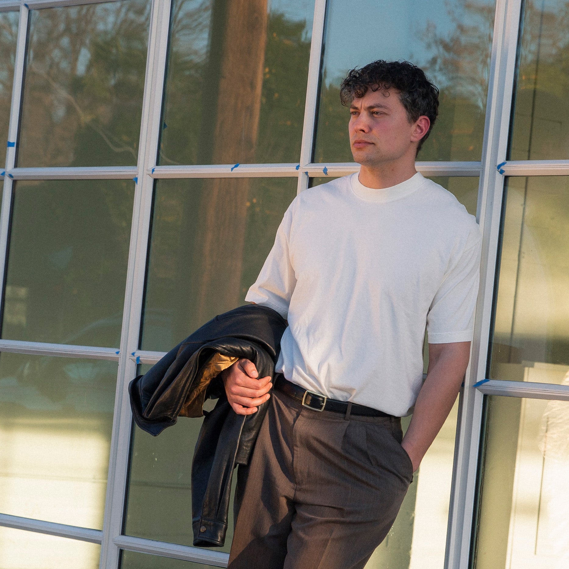 Man holding a jacket in front of a glass building. Upper Park Clothing Basic White Tees