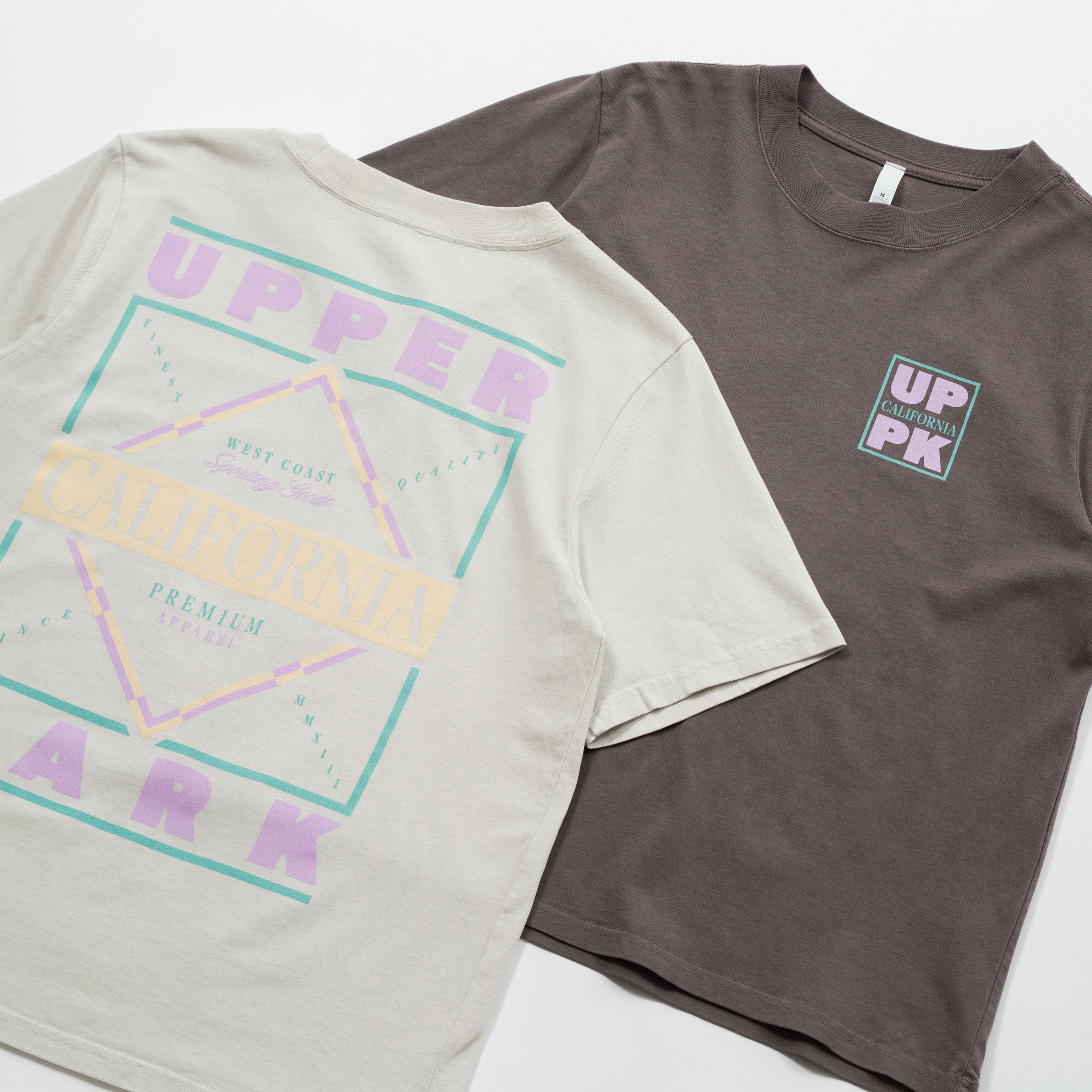 Upper Park Discovery Graphic Women's Tee - Two t-shirts, one gray with colorful graphics and text, the other brown with a logo, on a white background.