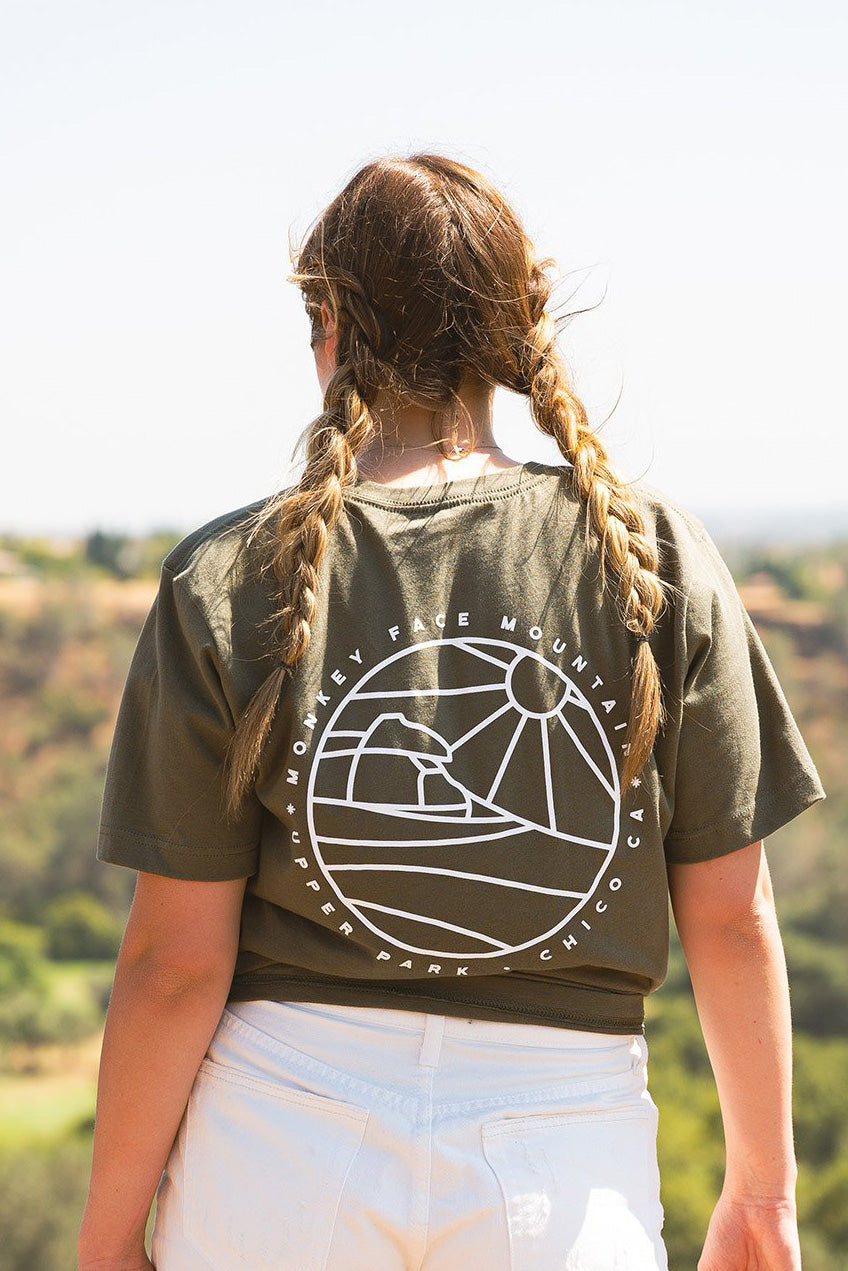 woman standing on top of monkey face rock looking out at the view. she is wearing white shorts with two braids in her hair modeling upper park clothings monkey face monoline t-shirt in military green
