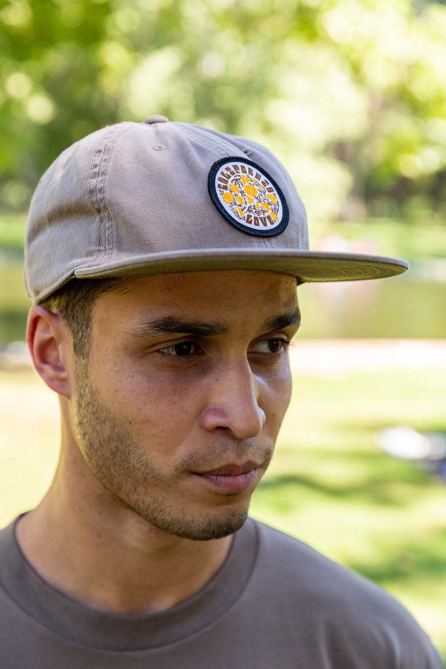 Man standing in Lower Bidwell park at One Mile pool in Chico, CA wearing a Upper Park Clothing James Cap with a California Poppy Love Patch