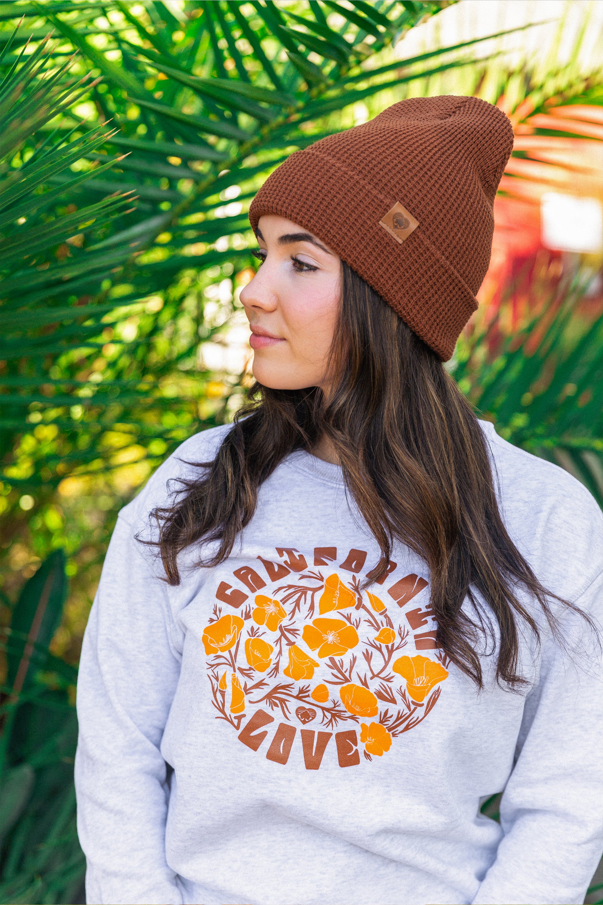 a women standing in a plant nursery wearing a California poppy love crew neck sweater ash colored from Upper Park Clothing in Chico California