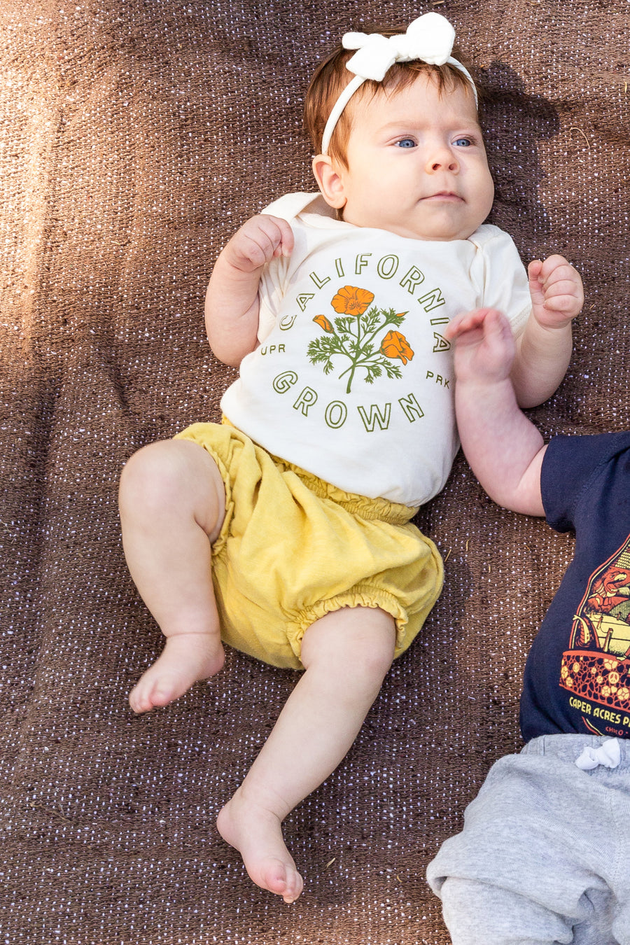 baby girl wearing a California Grown Onesie from Upper Park Clothing while laying on a blanket