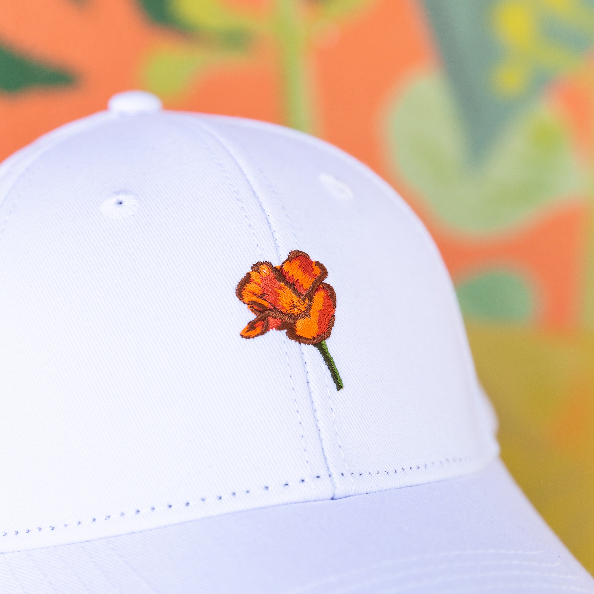 a white Upper Park Clothing California Poppy Hat sitting on a table infront of a colorful wall