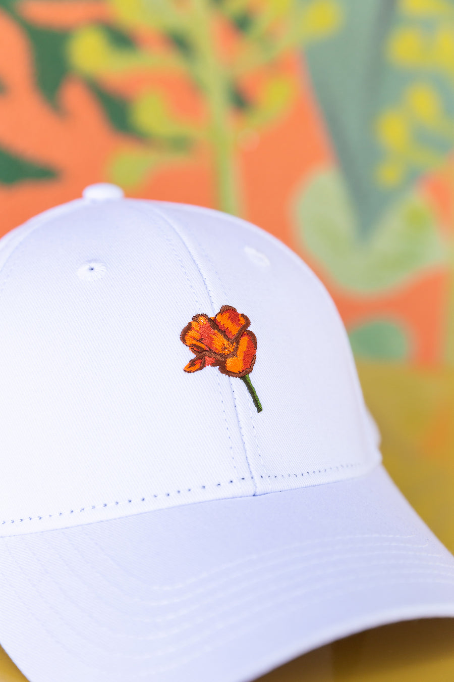 a white Upper Park Clothing California Poppy Hat sitting on a table infront of a colorful wall