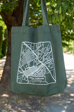 a Upper Park Clothing Chico Map Tote Bag hanging in front of a tree in the downtown streets of Chico