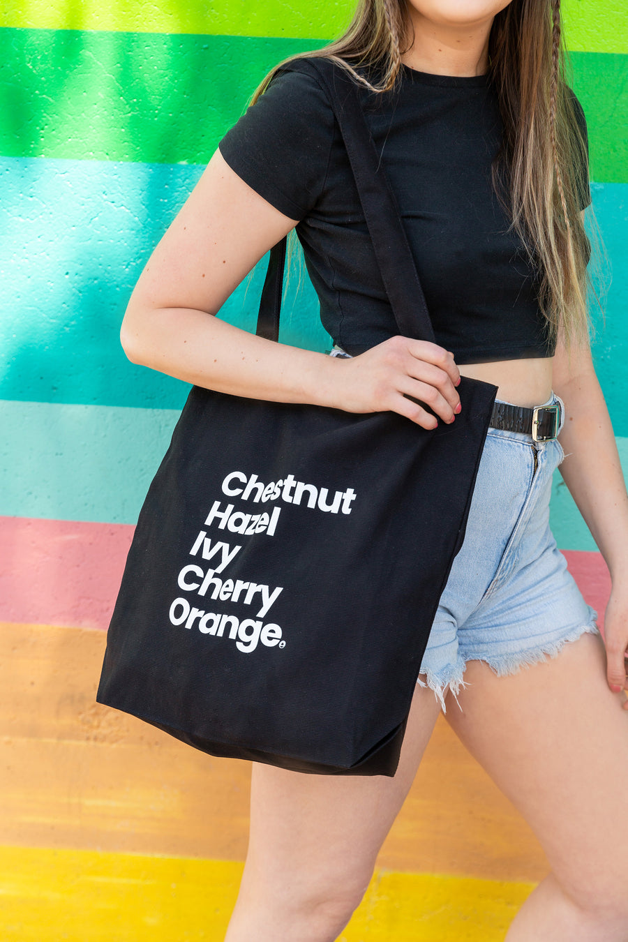 a Upper Park Clothing Downtown Streets Black Tote bag being held up infront of a rainbow wall in Downtown Chico