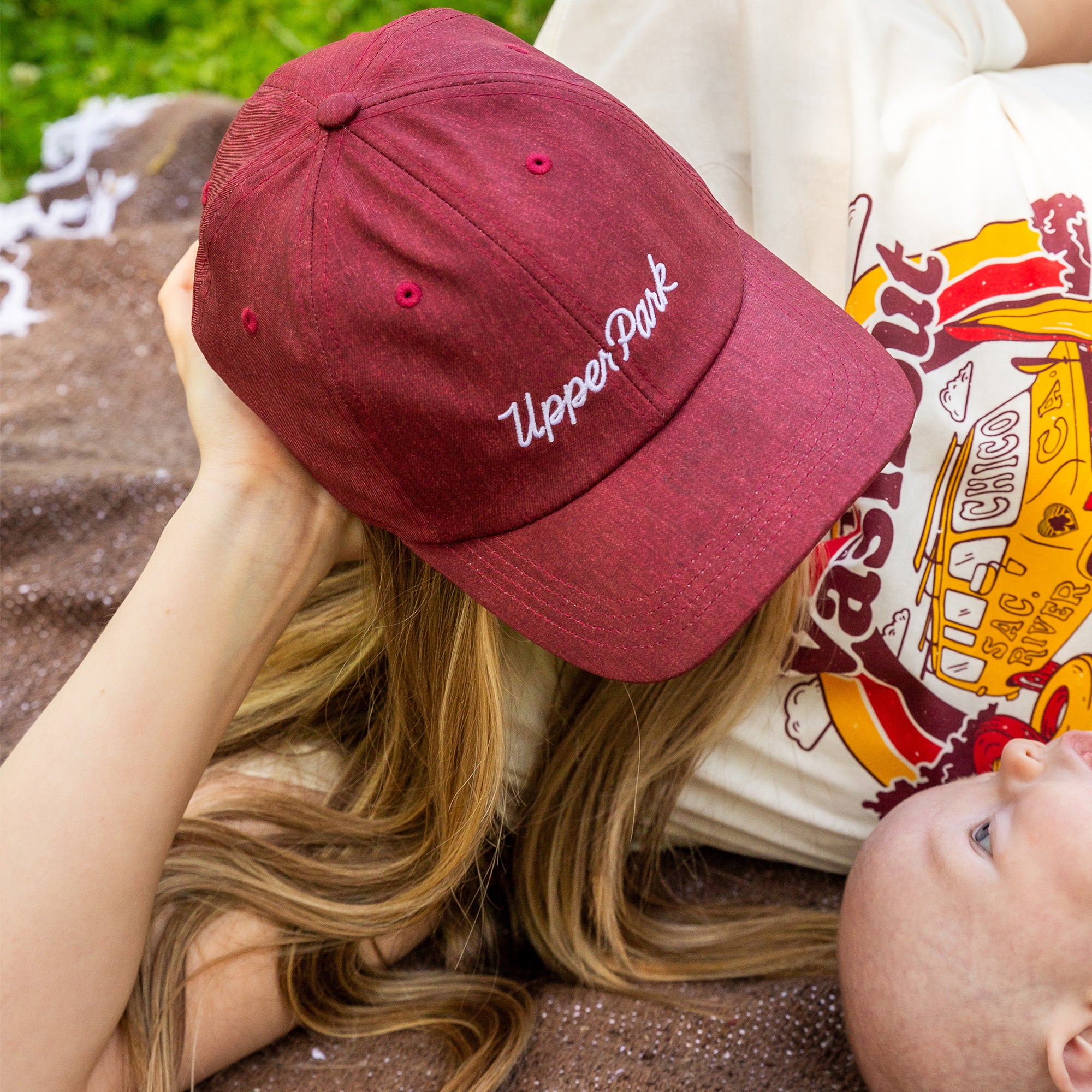 Mother and son laying on a Upper Park Clothing blanket wearing a performance hat while looking down at her son