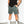 mean leaning against a white wall wearing a black pocket flag tee and green men's stadium shorts from Upper Park Clothing