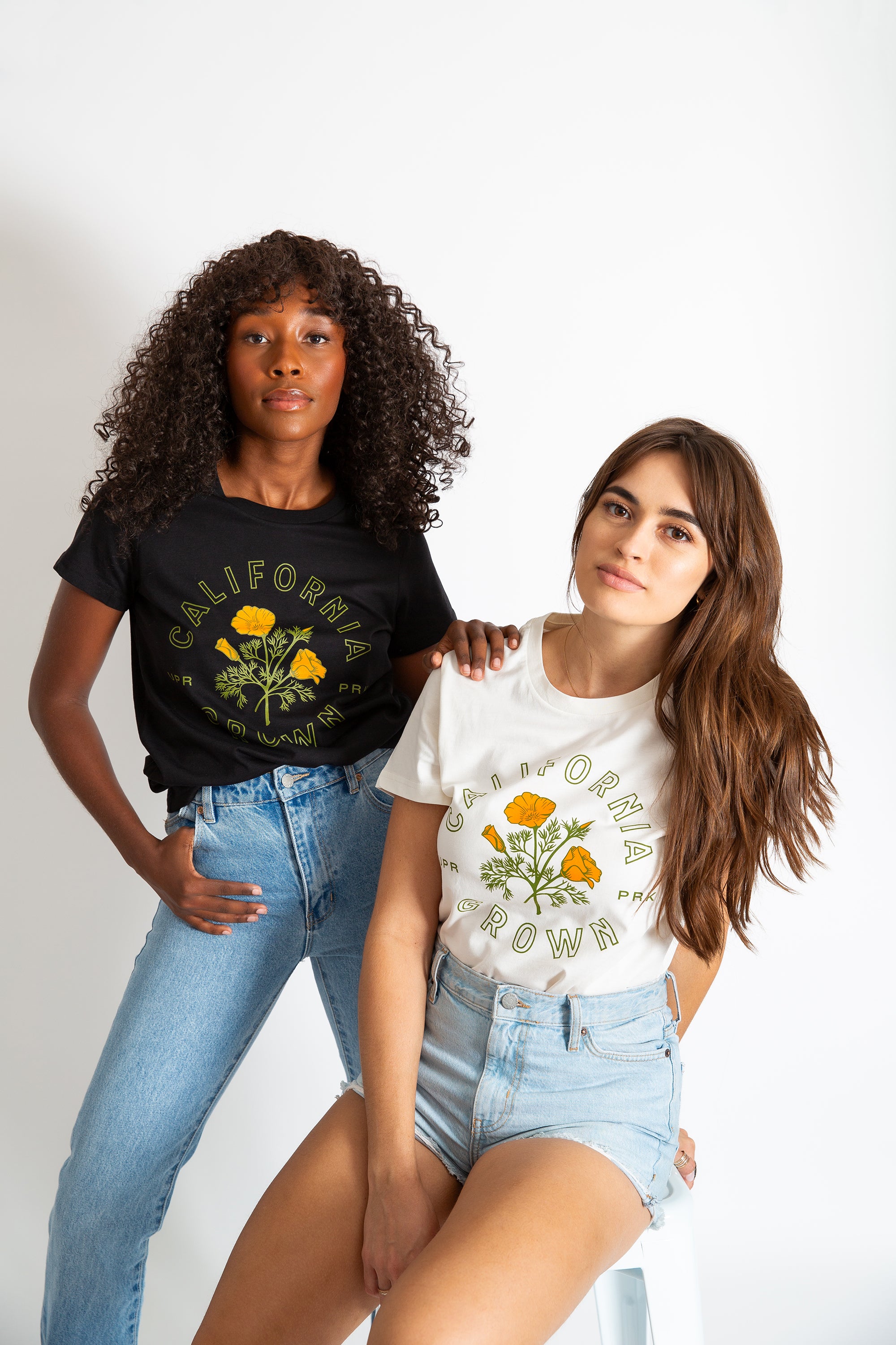 two women, one standing one sitting, in a studio photography setting wearing California Grown Routine Tees in Black and Natural from Upper Park Clothing in Chico California 