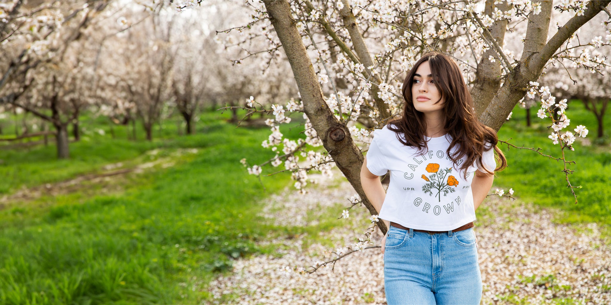 woman standing in a almond orchard wearing a white California Grown Crop Tee from Upper Park Clothing in Chico, CA