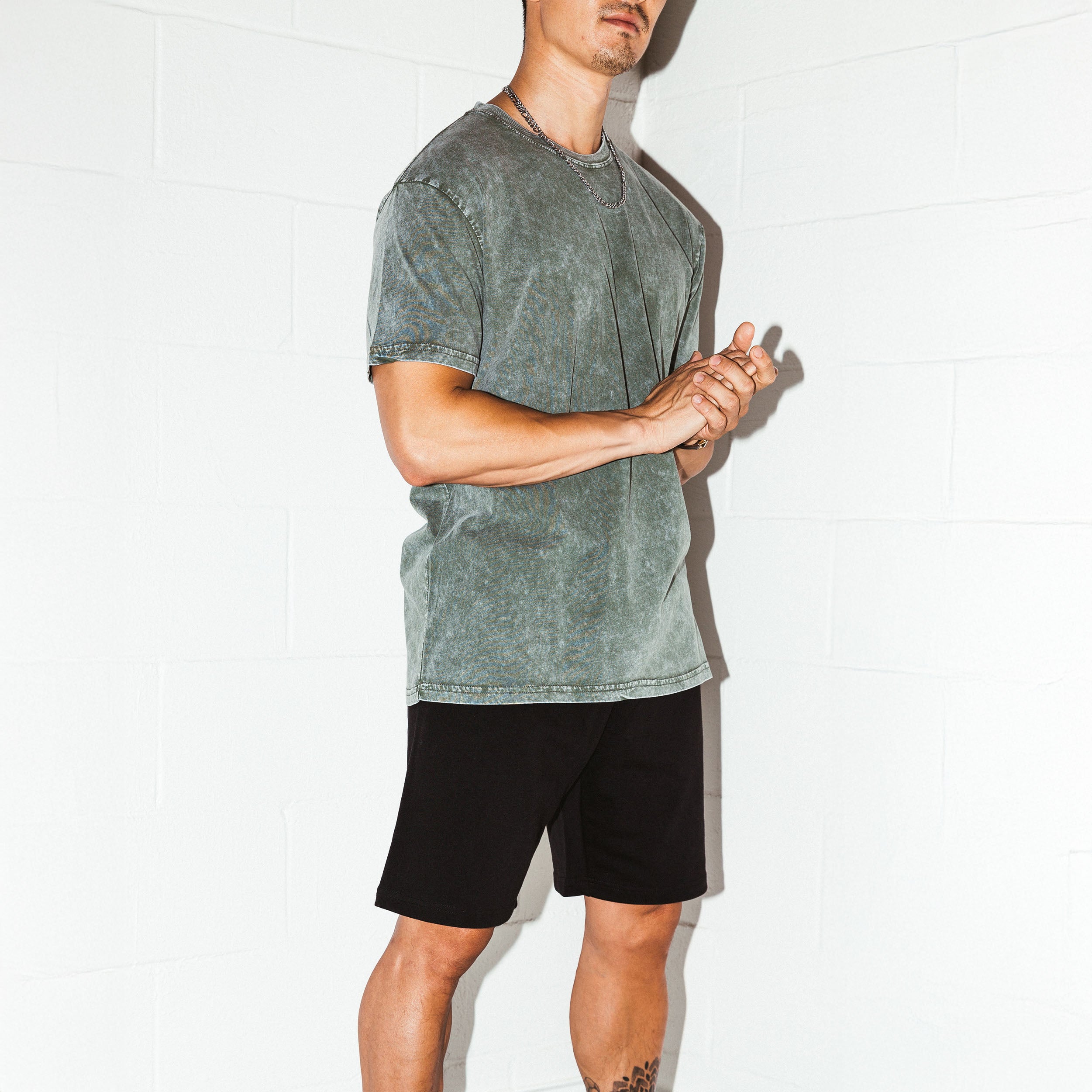 Person wearing a green t-shirt and black shorts against a white background. Upper Park Simple Stone Wash Tee