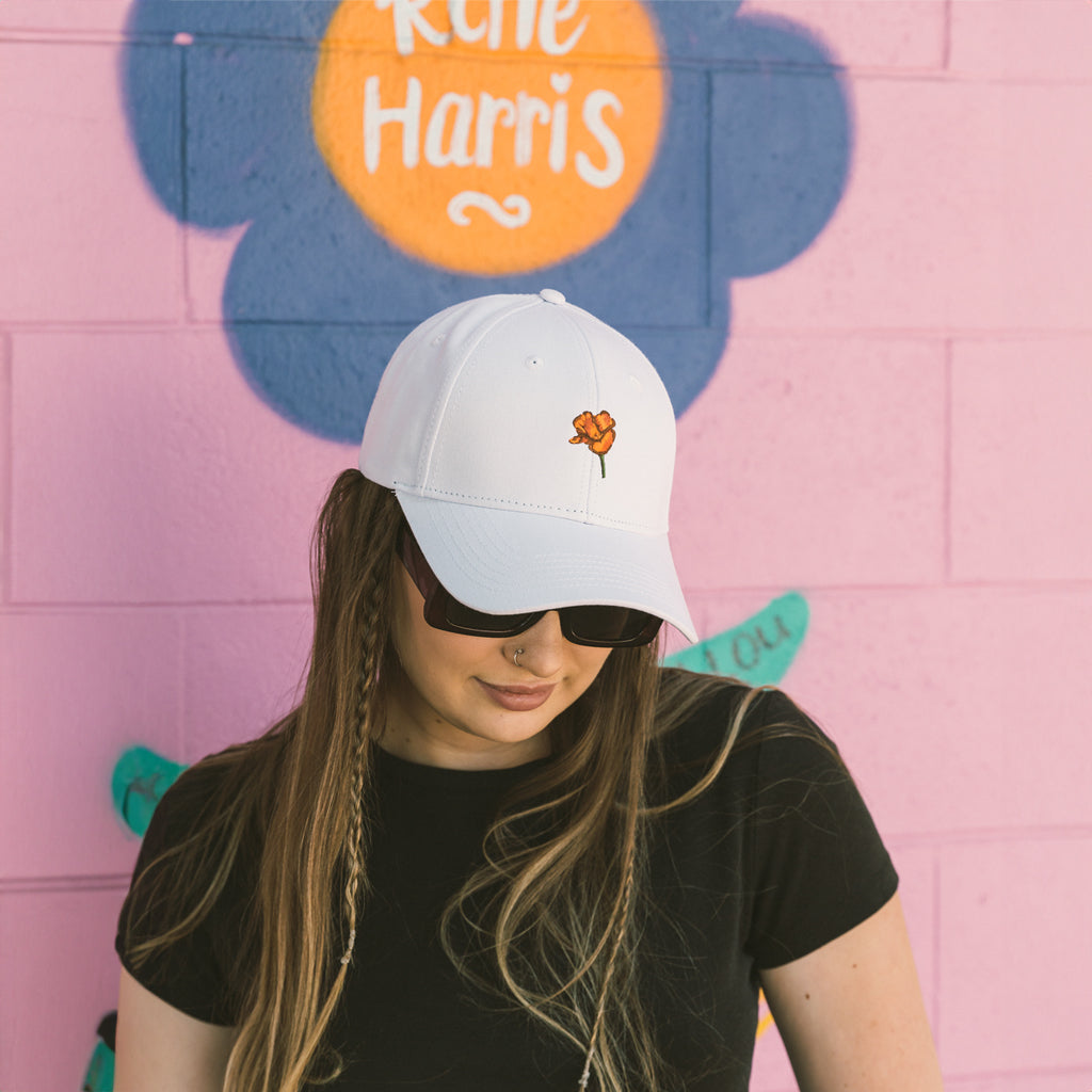 women standing in front of a pink wall wearing a California State Flower Poppy White Hat from Upper Park Clothing in Chico, California