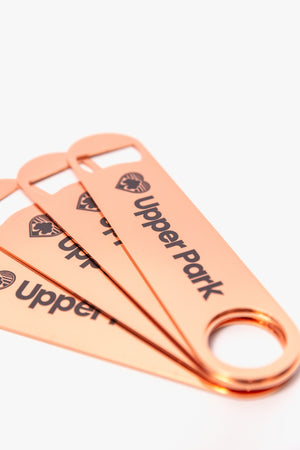 rose gold bottle opener with giant text that says "Upper Park" laying on a flat grey background