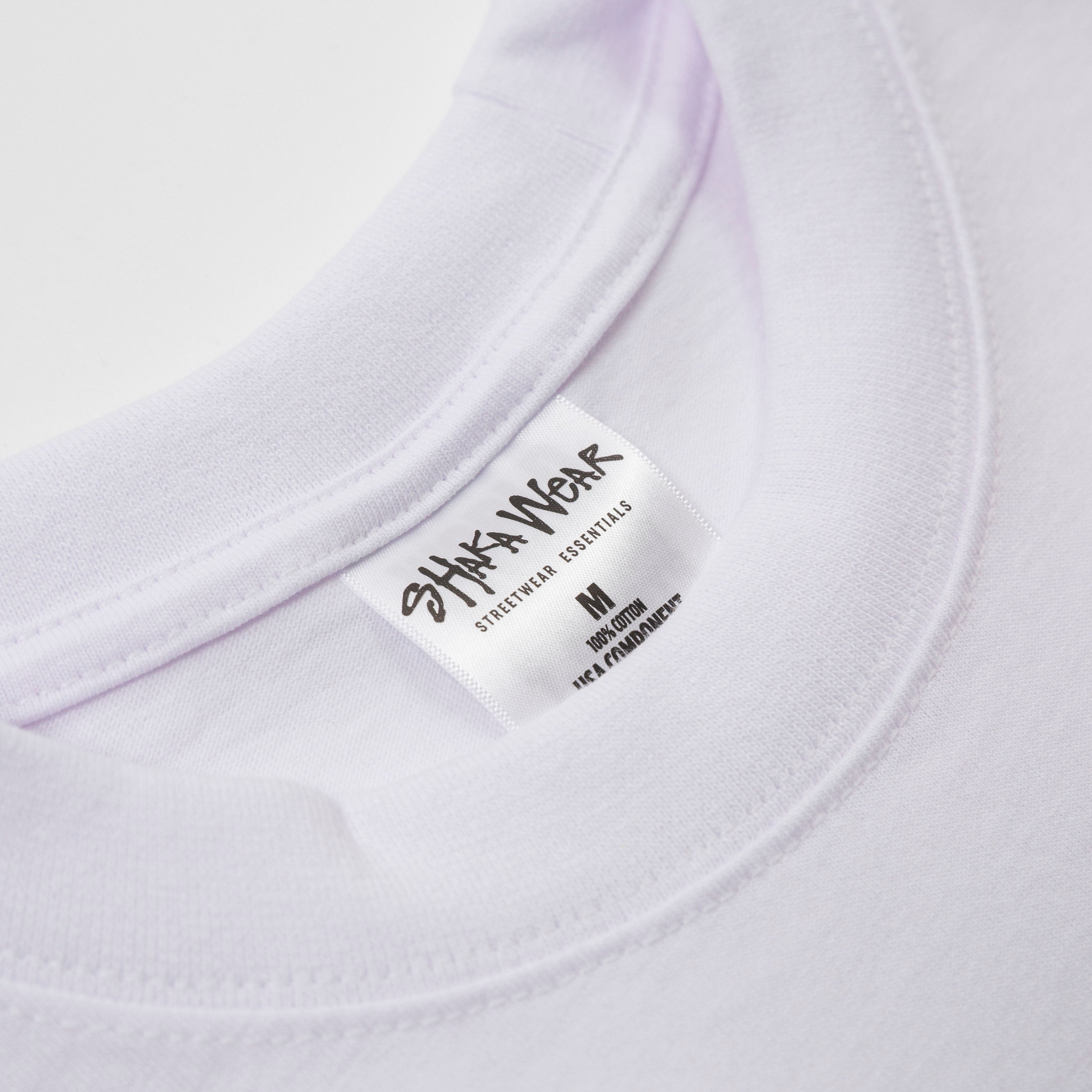 Close-up of the collar of a white shirt with a Shaka Wear label on a light gray background - Shaka Wear 7.5oz Heavyweight Cotton Tee