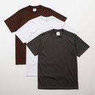Three plain t-shirts in brown, white, and black on a light gray background - Shaka Wear 7.5oz Heavyweight Cotton Tee
