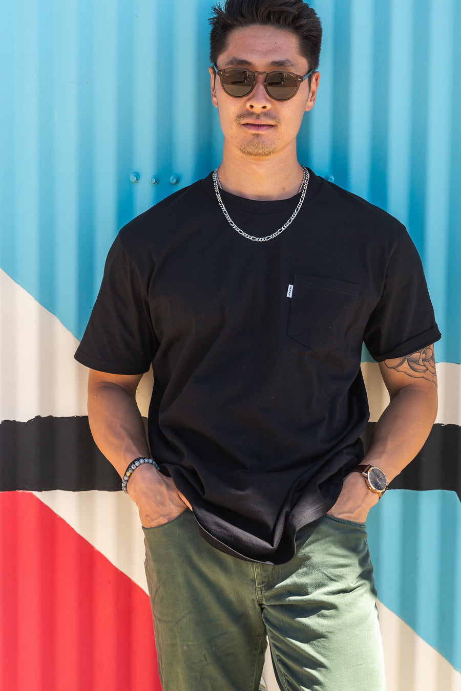 mean leaning against a painted wall wearing a black pocket flag tee from Upper Park Clothing