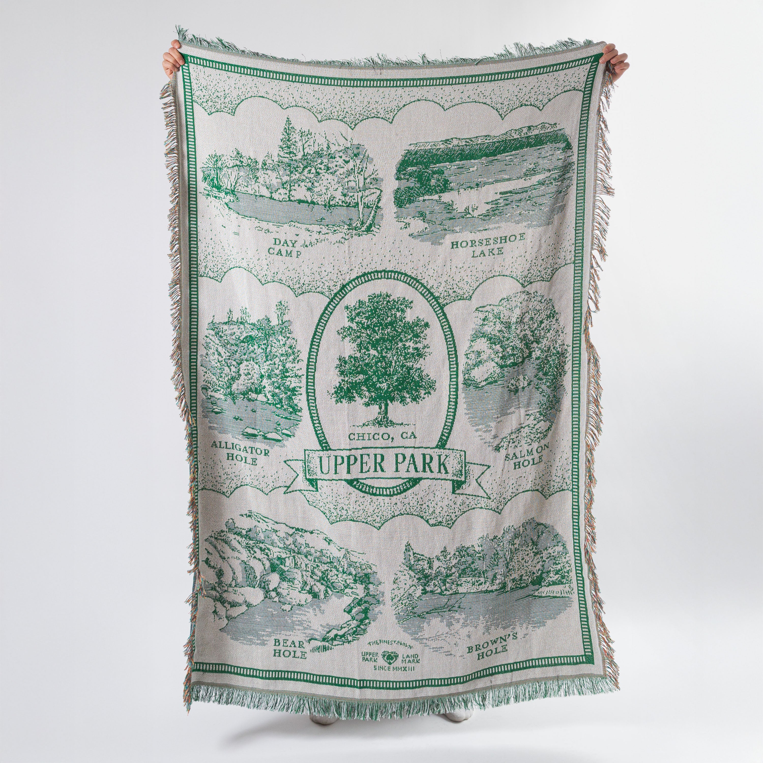 Green and white patterned blanket with scenic designs held by a person on a white background - Upper Bidwell Park Woven Blanket