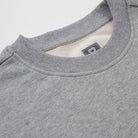 Close-up of a gray sweatshirt with a brand label on the collar against a light gray background - Basics Premium Cotton Sweater