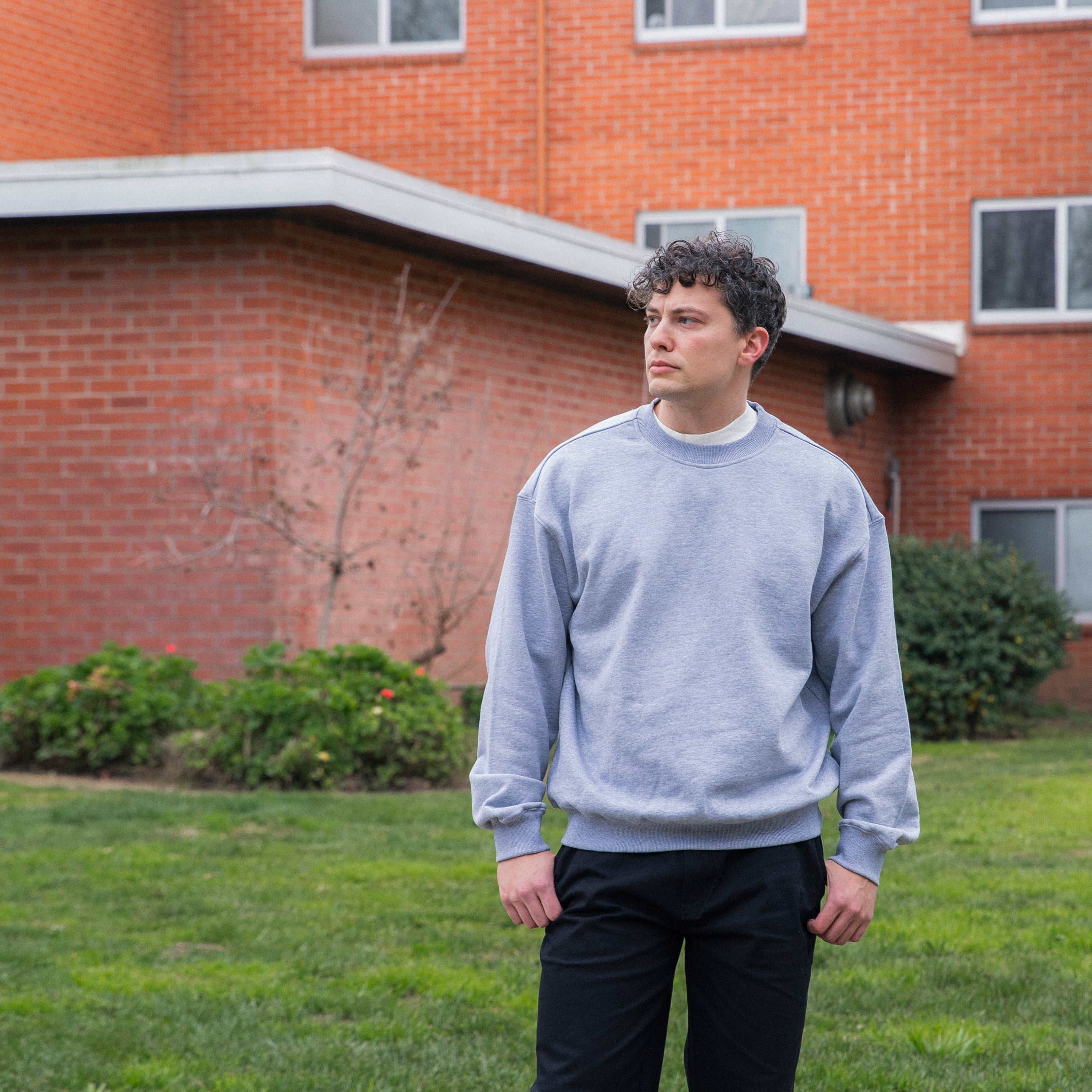Person wearing a gray sweatshirt standing in front of a brick building - Basics Premium Cotton Sweater