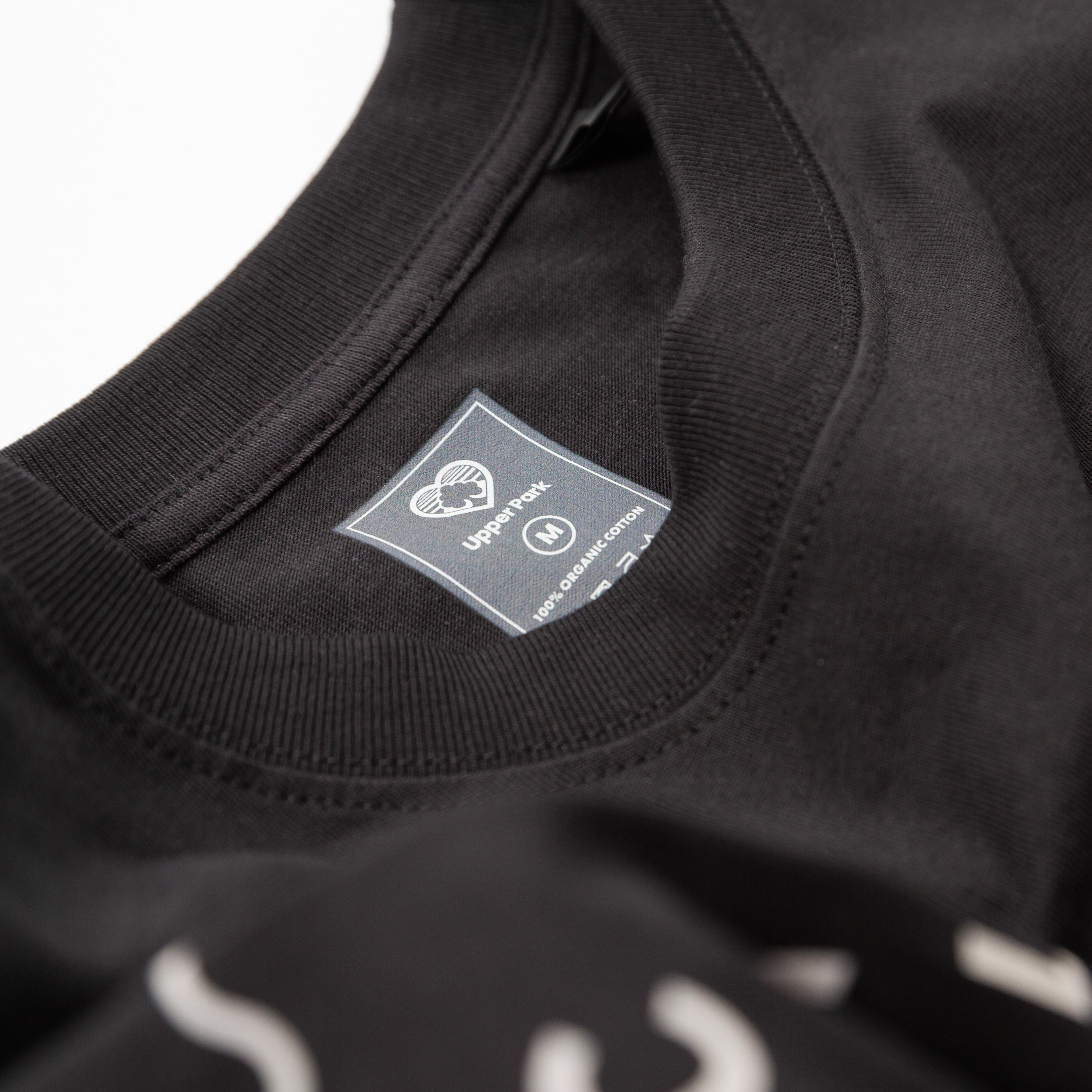 Upper Park Bay Waves Organic Cotton Long Sleeve shirt - Close-up of a black garment with a label on a white background