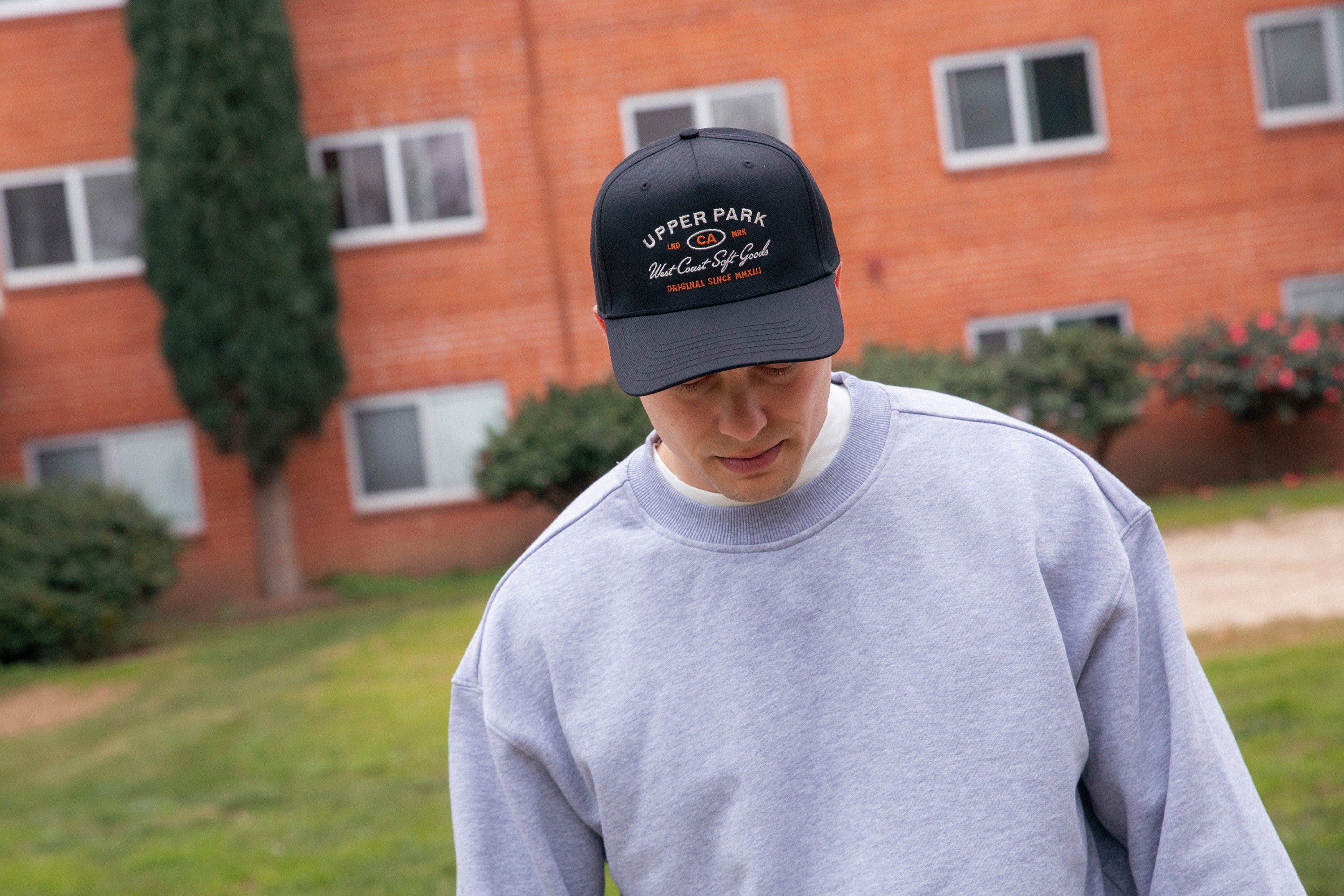Person wearing a gray sweatshirt and black cap with 'Upper Park' logo outdoors.