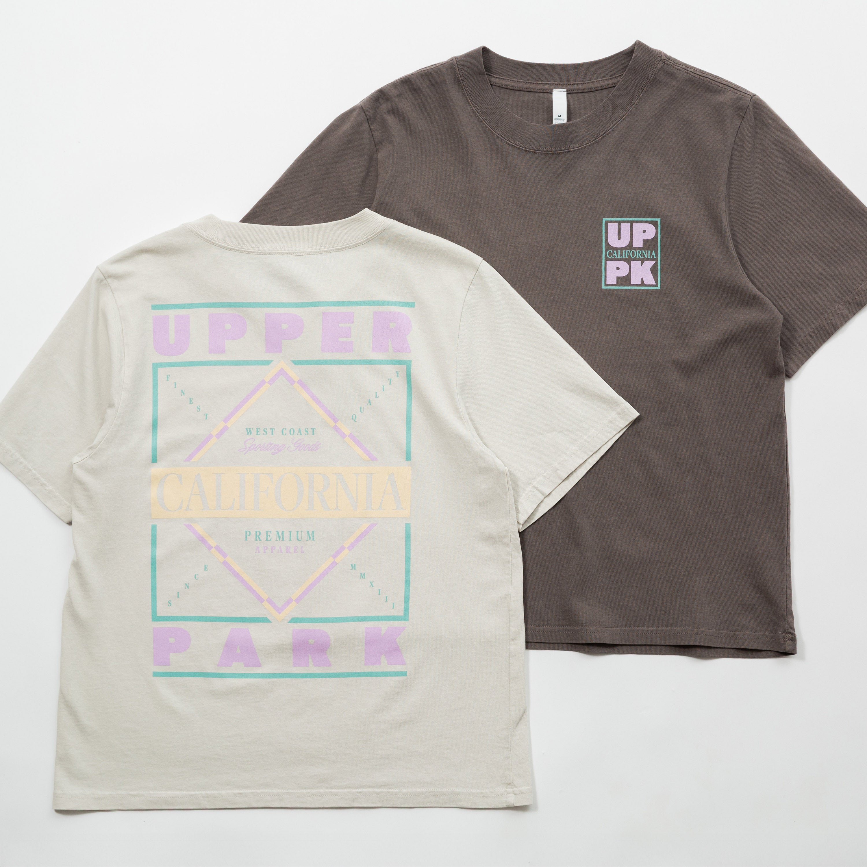 Upper Park Discovery Graphic Women's Tee - Two t-shirts, one gray with a logo on the chest and one beige with a geometric design, on a white background.
