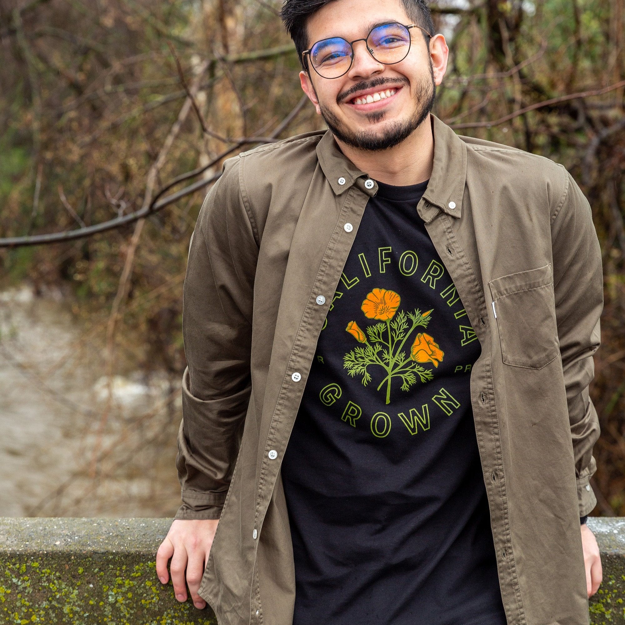 Man wearing a black California Grown shirt from Upper Park Clothing while standing on a bridge in Bidwell Park, Chico, Ca