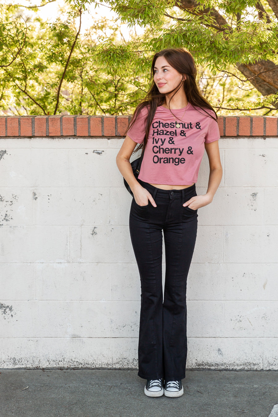 women standing on front of a white brick wall wearing a mauve colored crop tee from Upper Park Clothing
